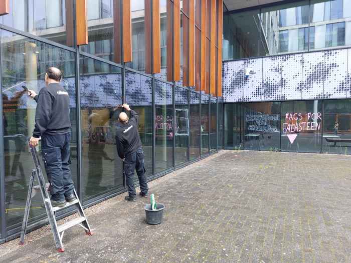 Photo of two cleaners who clean up a wall of a building at Science Park